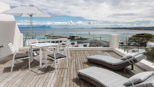 A wooden deck with a table and chairs, a white umbrella, and two lounge chairs with cushions. - First Group Cape Gordonia (Cape Town)