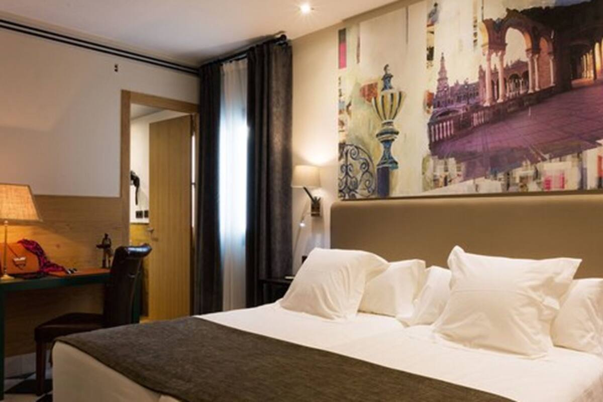 Ein Hotelzimmer mit Bett, Schreibtisch und Stuhl. Ein Gemälde hängt an der Wand, auf dem Schreibtisch steht eine Lampe.