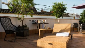 A terrace with wicker furniture, a small table with bottles, and a potted plant. - Aguilas5 SevillaSuites (Seville)