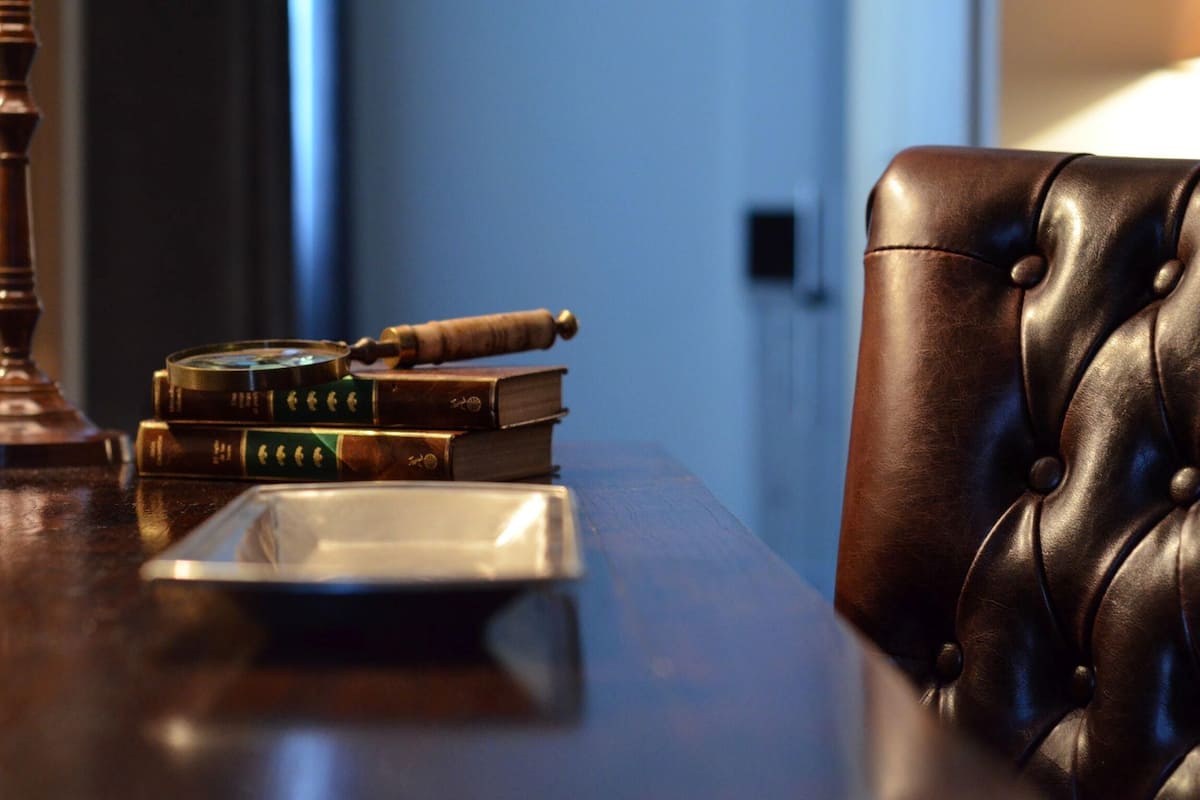 Ein Ledersessel, ein Bücherstapel und eine Lupe auf einem Holztisch.
