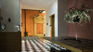 A lobby with a checkered floor, a reception desk, a decorative plant, and a wall with a classical architectural design. - Aguilas5 SevillaSuites (Seville)