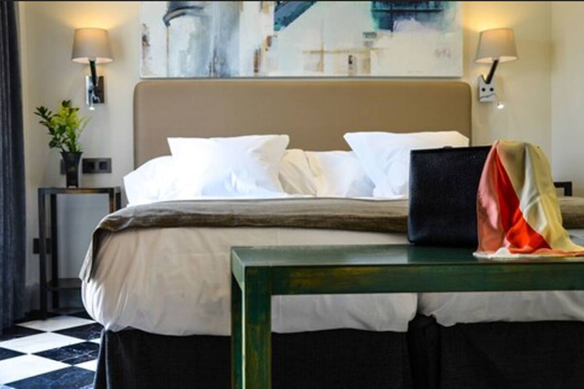 Ein Hotelzimmer mit einem Bett, zwei Nachttischlampen, einem Bild an der Wand, einem kleinen Tisch mit Decke und einem karierten Boden.