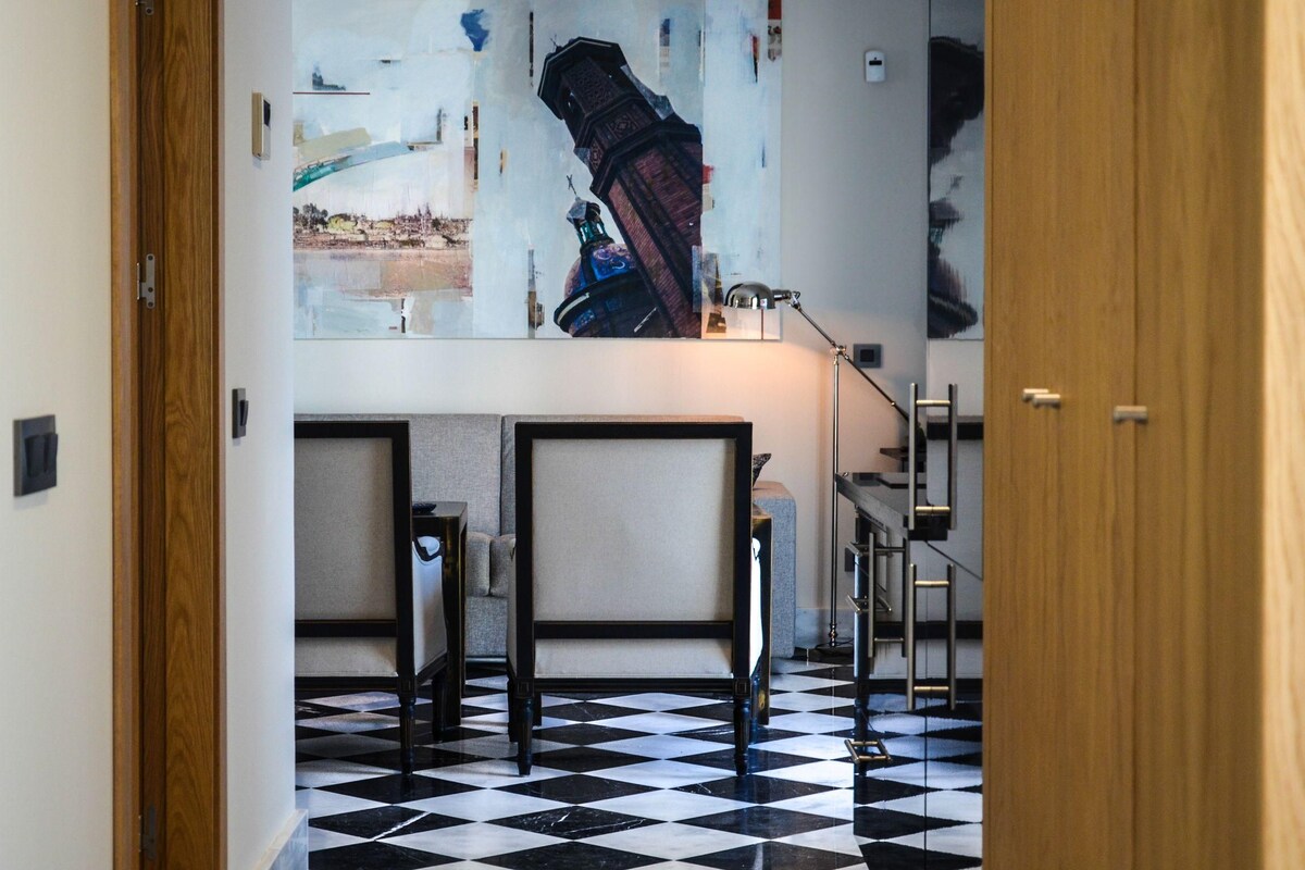 A hallway with a checkered floor, a painting on the wall, and a staircase.