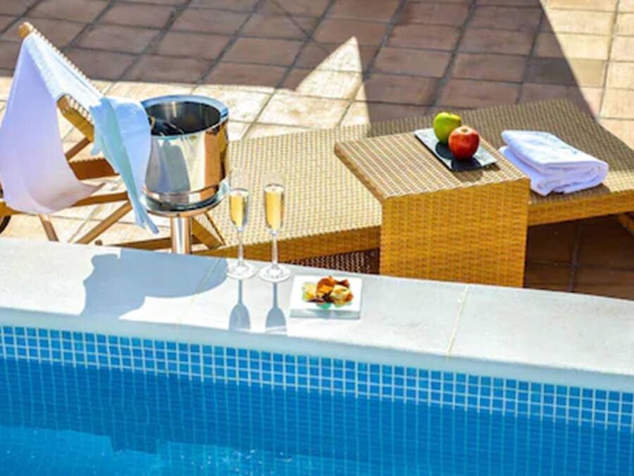 A poolside setting with a sun lounger, a bucket, a plate of fruit, and a glass of champagne.