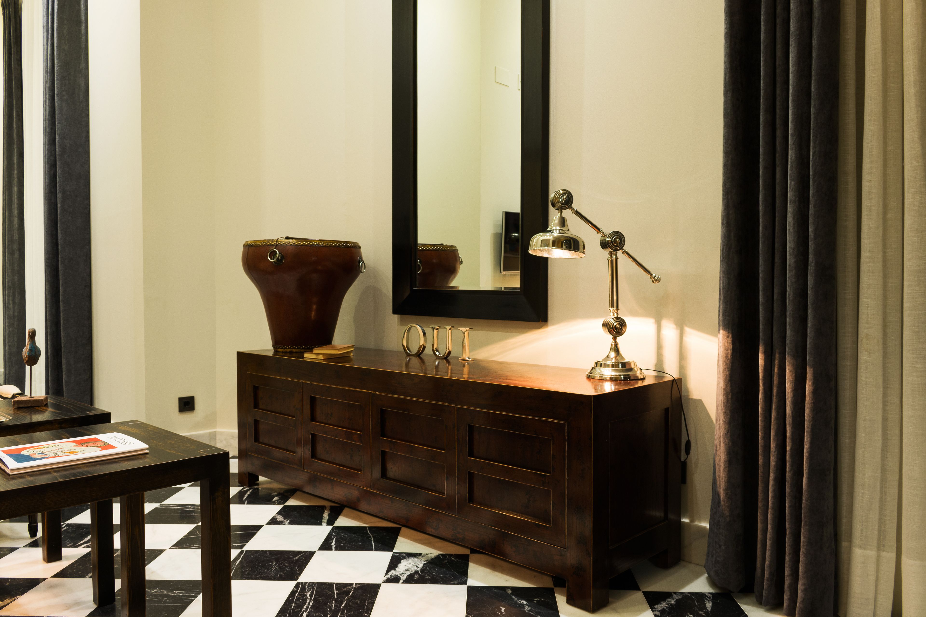 A room with a checkered floor, a wooden vanity with a mirror, a lamp, and a vase.