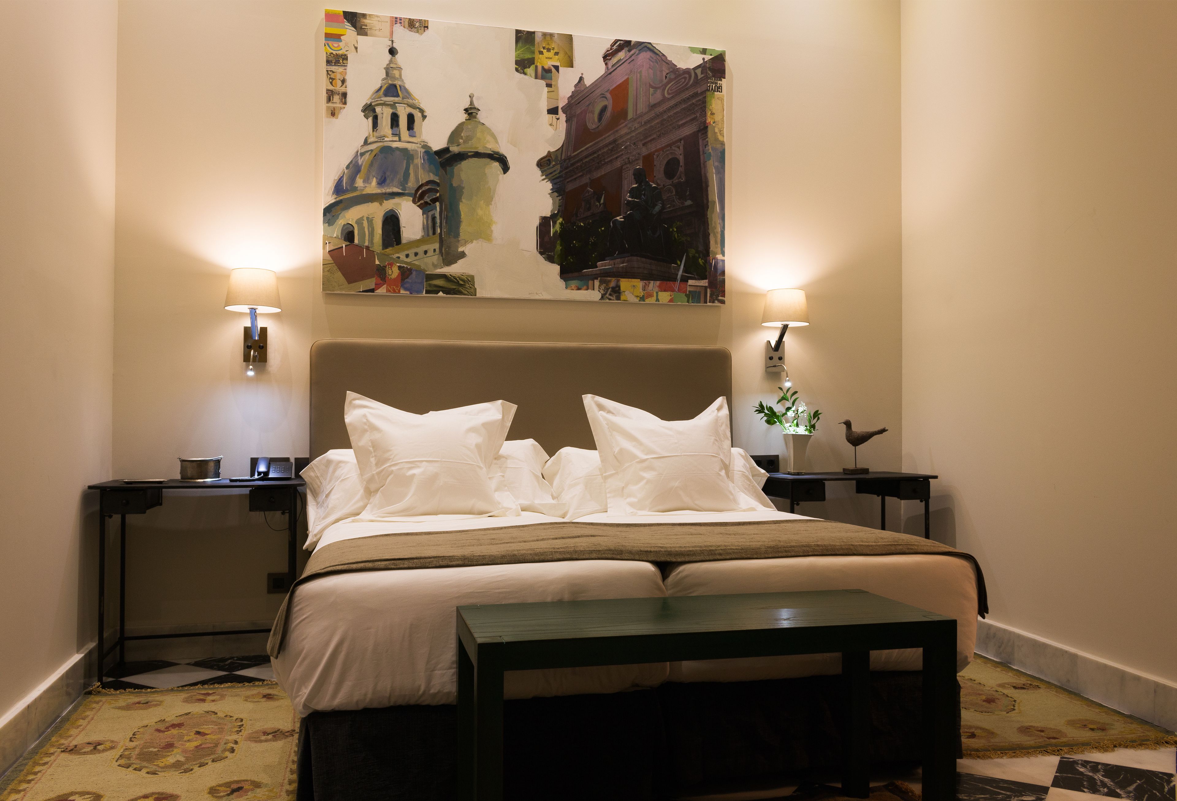 A hotel room with a large bed, two bedside tables, a nightstand, a desk, and a painting on the wall.