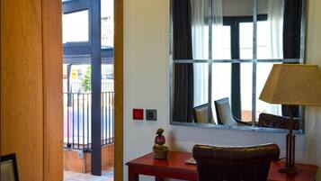 A hotel room with a wooden door, a window with curtains, a table with a lamp, and a small statue.