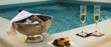 A poolside setting with a metal bowl containing bottles and glasses, and two glasses of champagne on a tray.