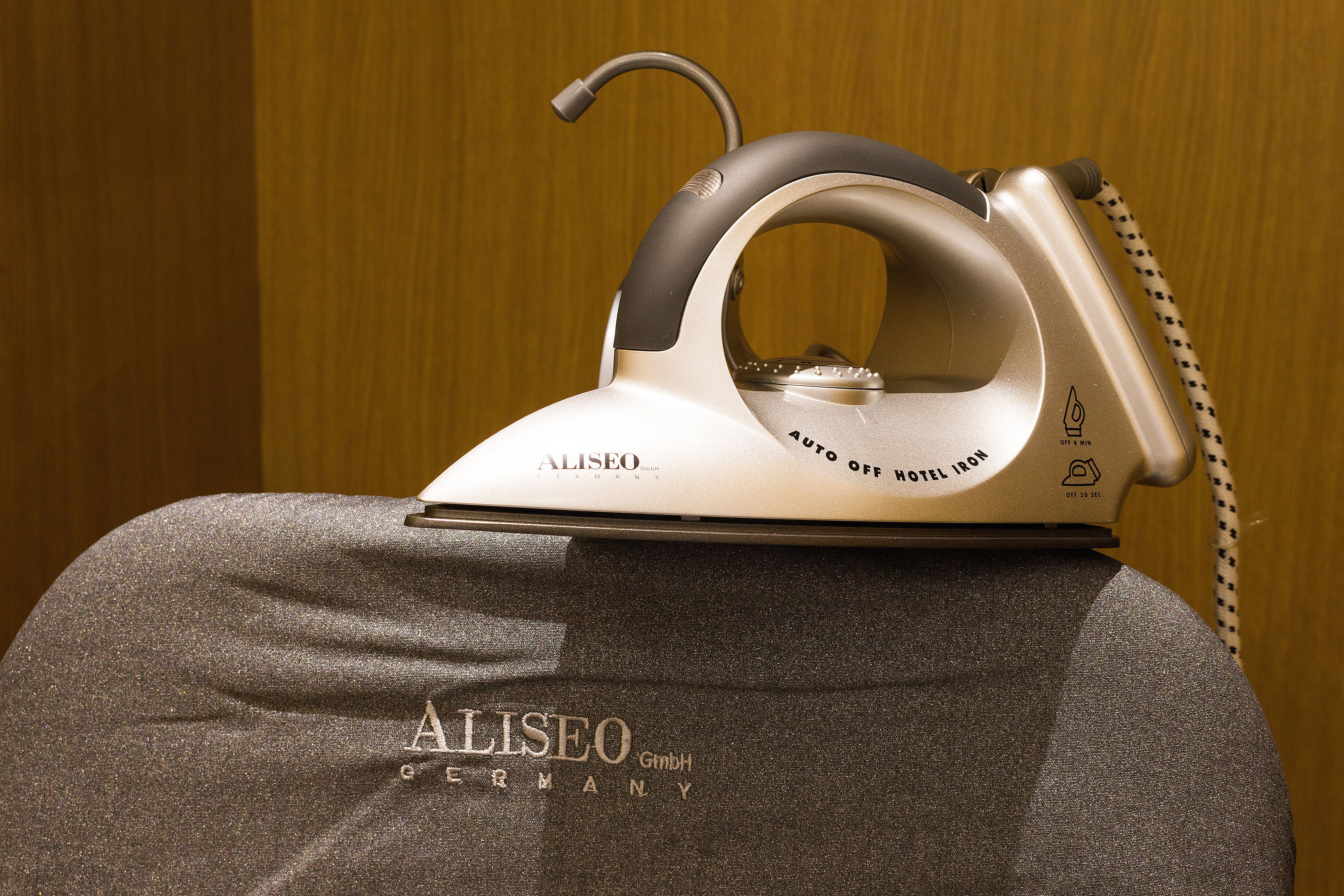 A modern, metallic iron with the brand name "ALISEO" on a textured fabric surface.