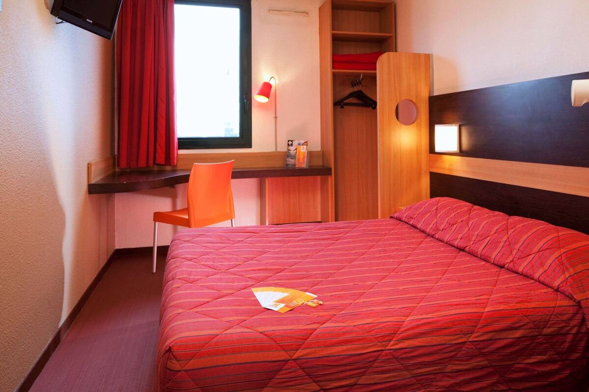 Ein Hotelzimmer mit einem Bett, einem Schreibtisch, einem Sessel, einem Kleiderschrank und einem an der Wand befestigten Fernseher.