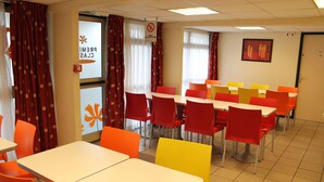 A dining area with tables and chairs in red, yellow, and orange colors. - Premiere Classe Saint Ouen L'Aumone (Saint-Ouen-l'Aumone)