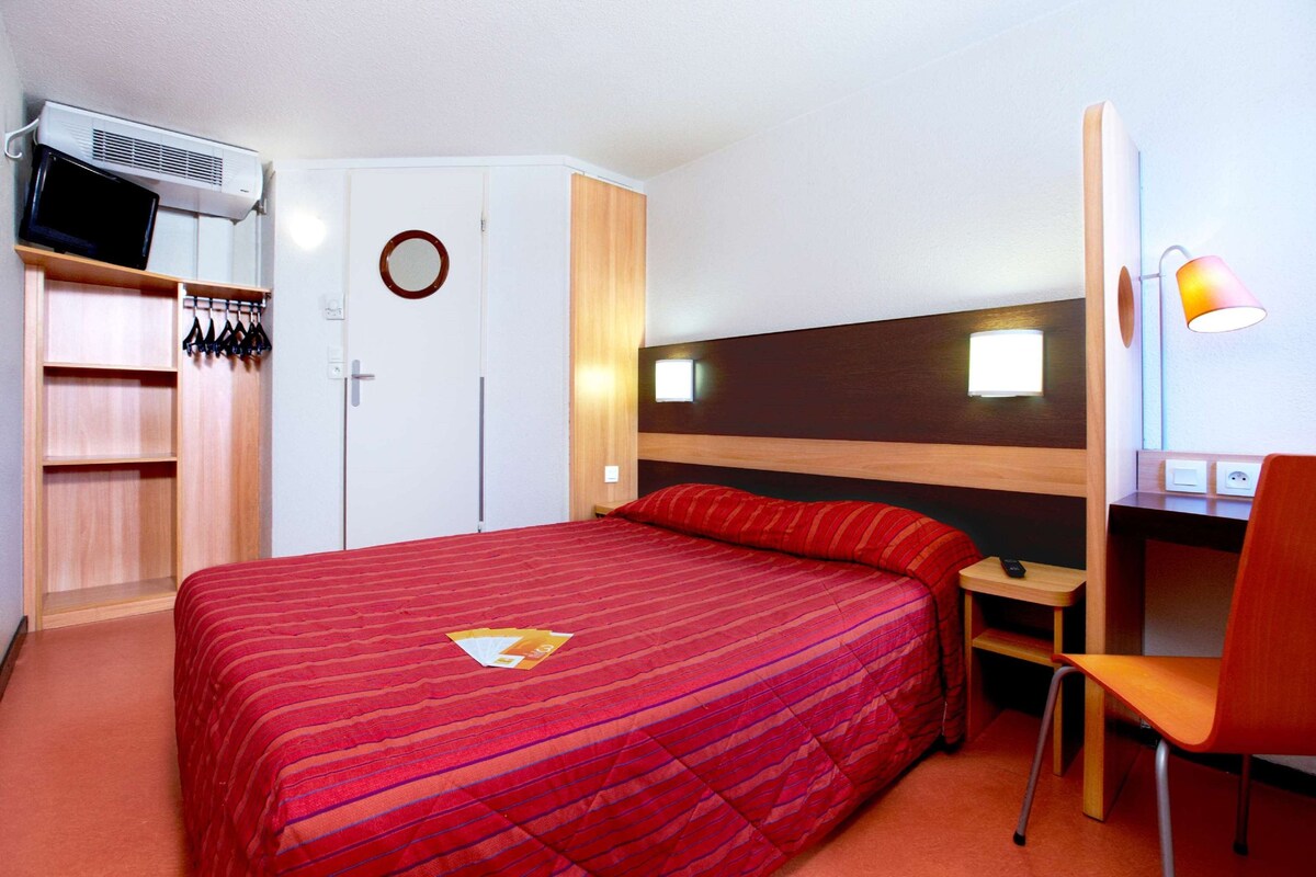 A hotel room with a bed, a desk, a chair, a TV, and a wardrobe.
