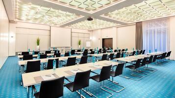 A conference room with long tables, black chairs, and a blue carpet.