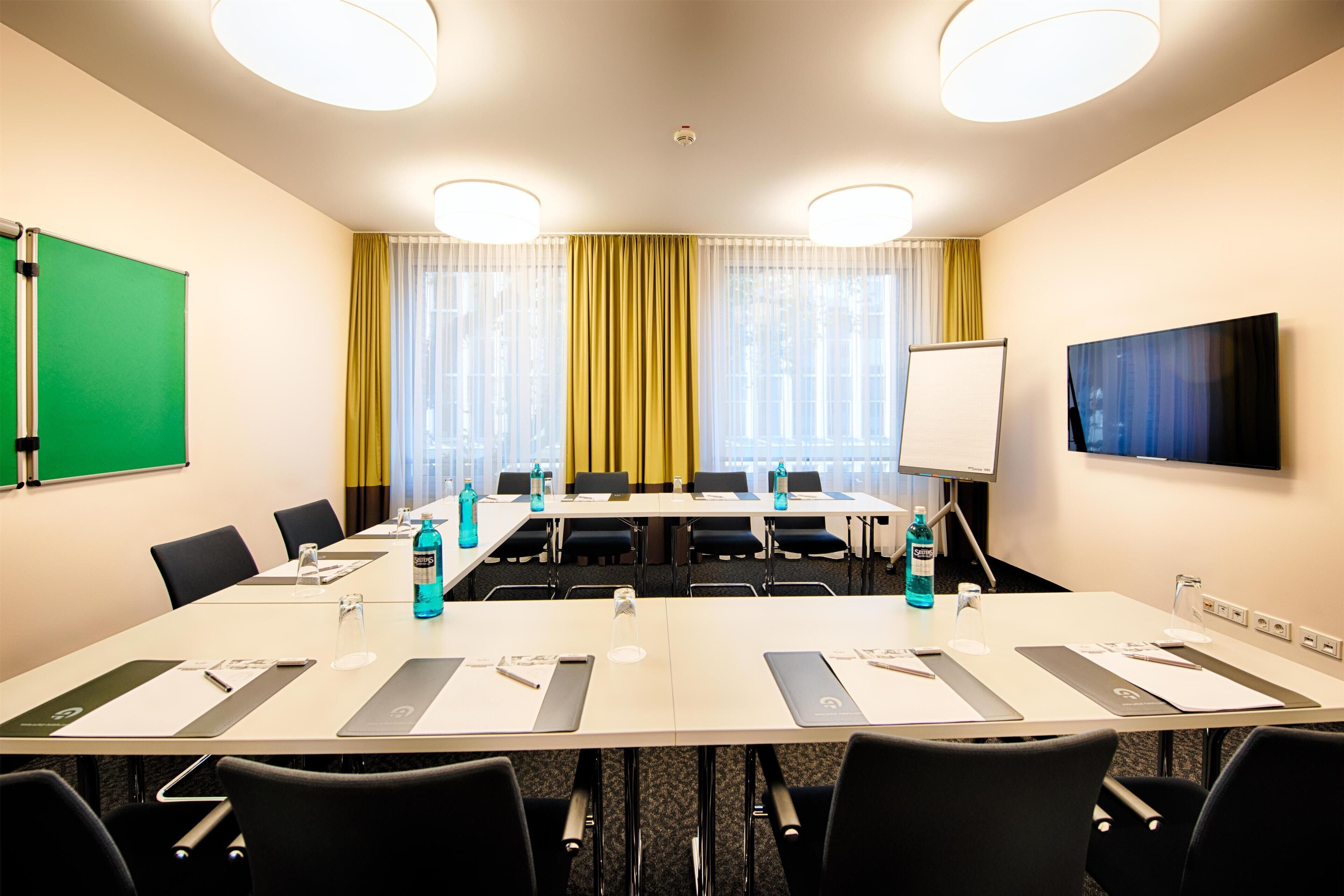 A conference room with a long table, chairs, a whiteboard, and a projector screen.