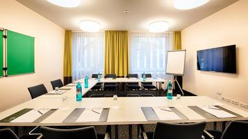 A conference room with a long table, chairs, a whiteboard, and a projector screen.