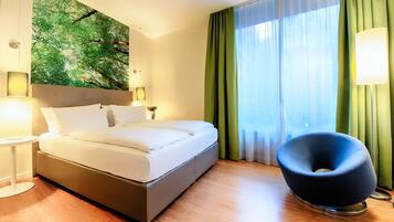 Een moderne hotelkamer met een bed, een ronde fauteuil, een wandlamp en een groot raam met transparante gordijnen.
