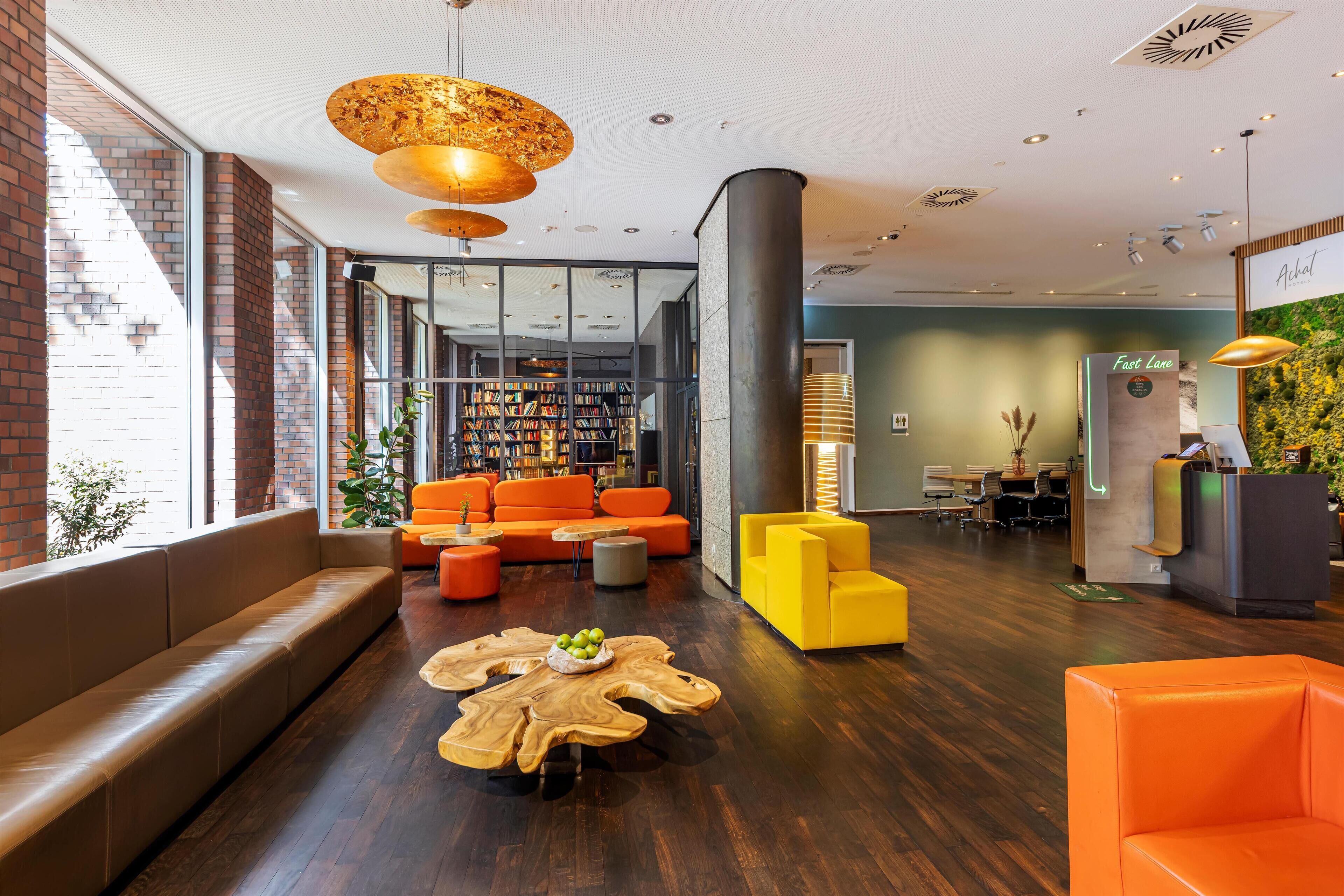 A modern lobby with a brick wall, a bookshelf, orange seating, and a reception desk.