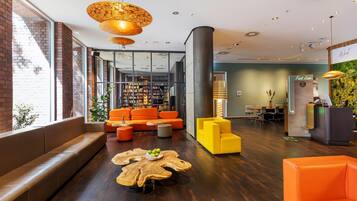 A modern lobby with a brick wall, a bookshelf, orange seating, and a reception desk.
