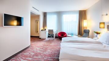 Hotelkamer met een groot bed, een bureau, een rode stoel en een aan de muur bevestigde televisie.