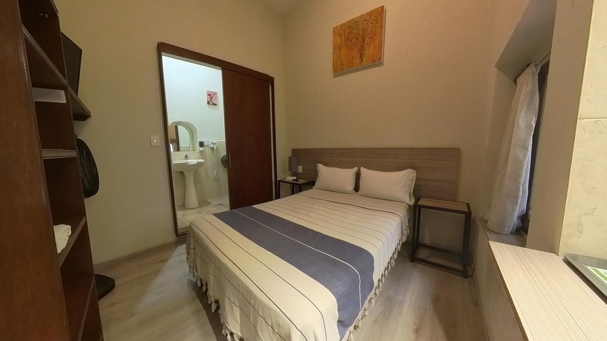 Une chambre à coucher avec un lit, des tables de chevet, une armoire et une salle de bain visible à travers une porte ouverte.