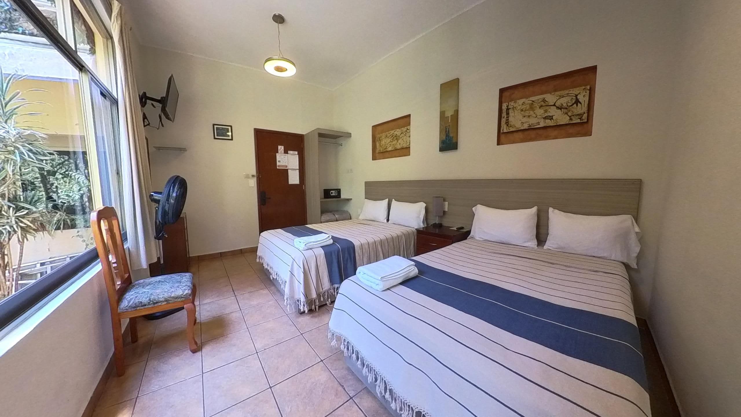 A hotel room with two beds, a chair, a desk, and a window.