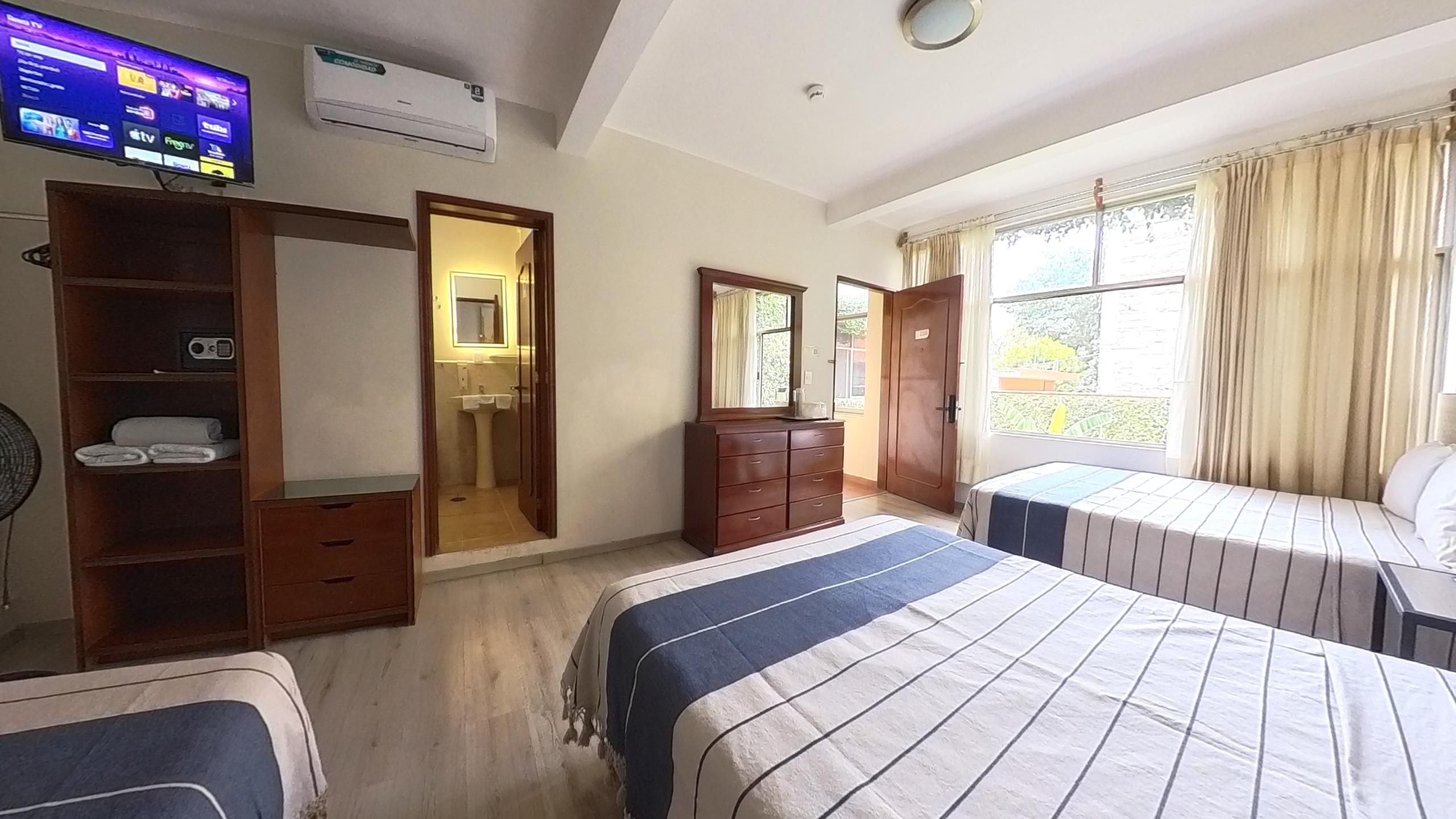 A hotel room with a bed, a dresser, a TV, and a window with curtains.