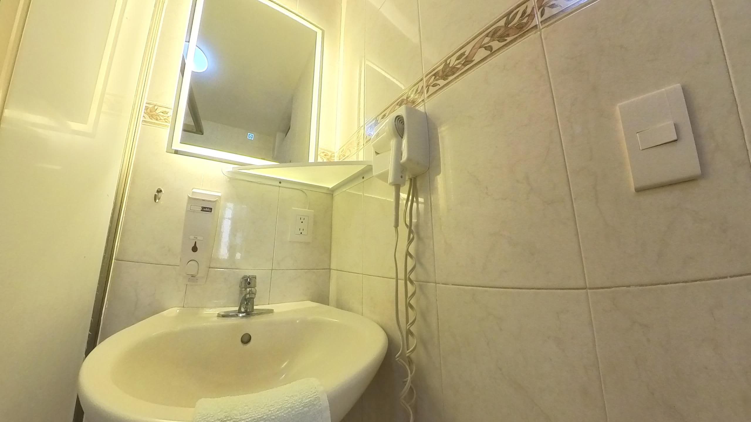 A bathroom with a sink, mirror, and a hairdryer on the wall.