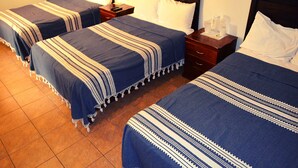 A hotel room with three beds, each with a blue and white striped bedspread. There are wooden nightstands with lamps and a small table with a pitcher and glasses. - Hotel Don Nino (Oaxaca)
