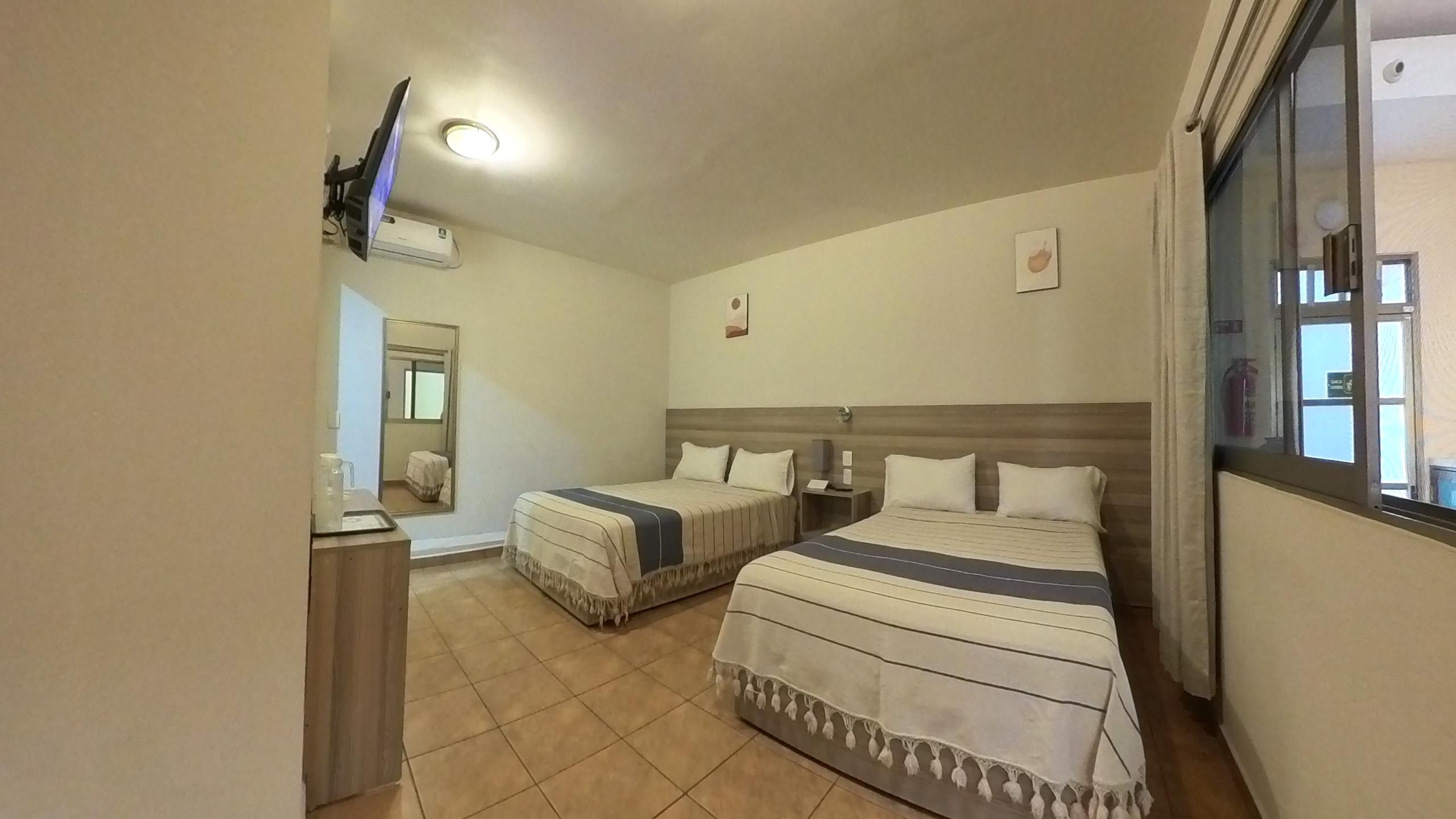Een hotelkamer met twee bedden, een kleintje tafeltje, een spiegel en een raam.