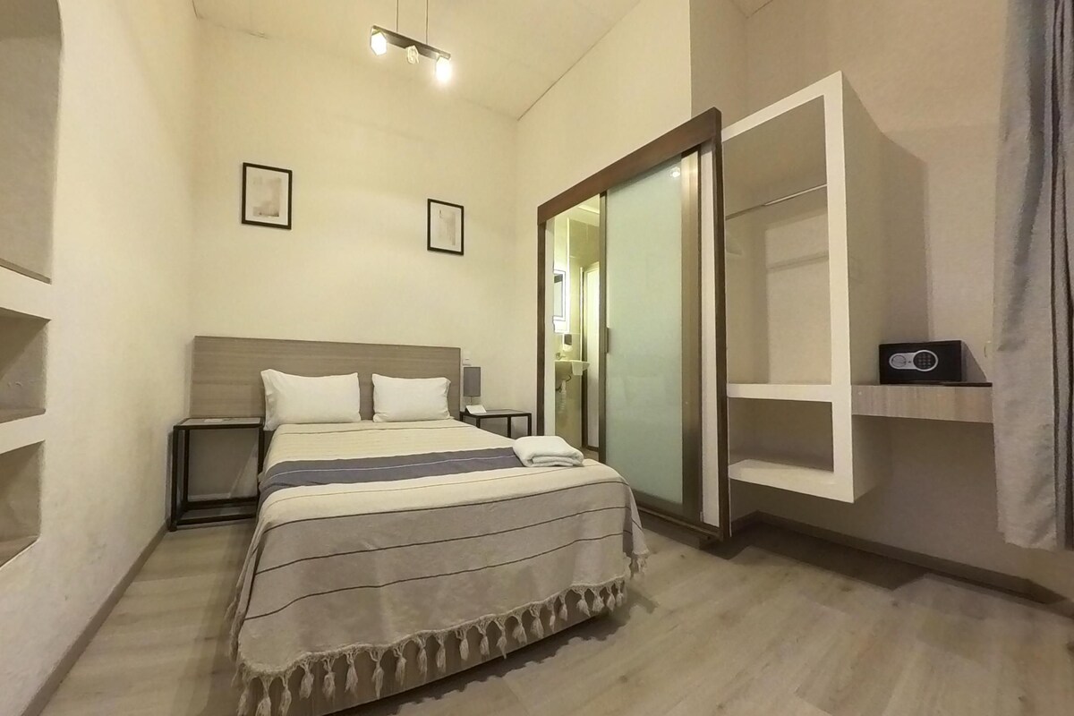 Un dormitorio con una cama, mesitas de noche, un armario y una estantería con un radio.
