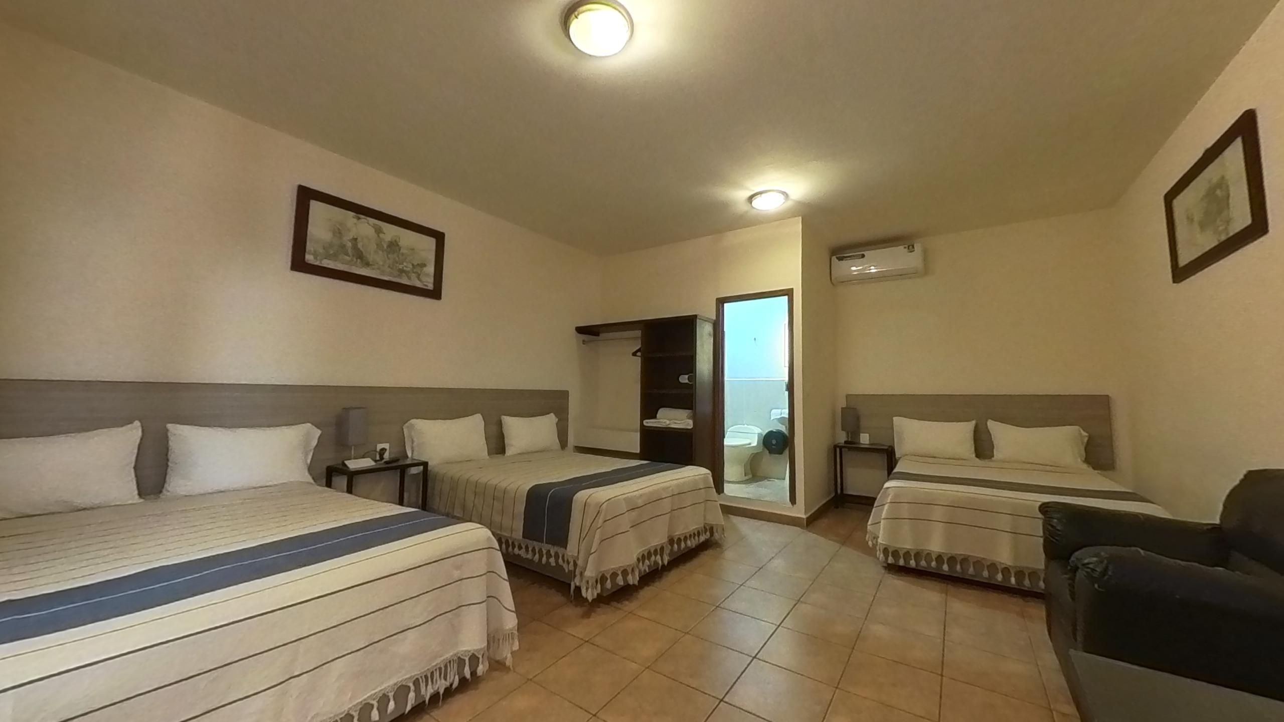 A hotel room with two beds, a small table, a chair, and a bathroom visible through an open door.