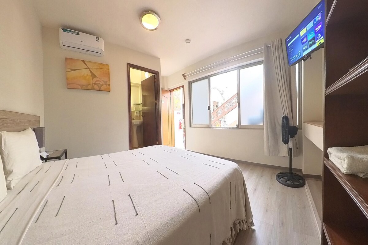 Una habitación de hotel con cama, televisor montado en la pared, ventana con vistas y aire acondicionado.