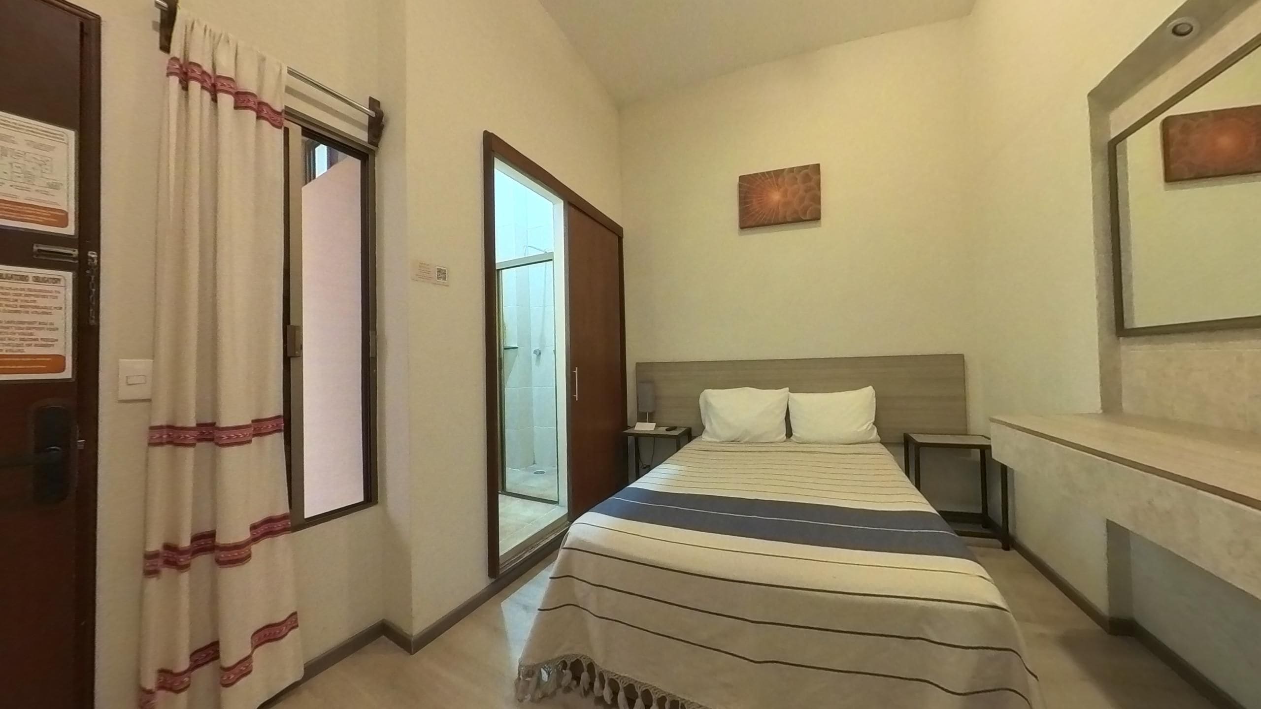 Habitación de hotel con cama, mesita de noche y un espejo, con puerta corredera que da a un balcón.