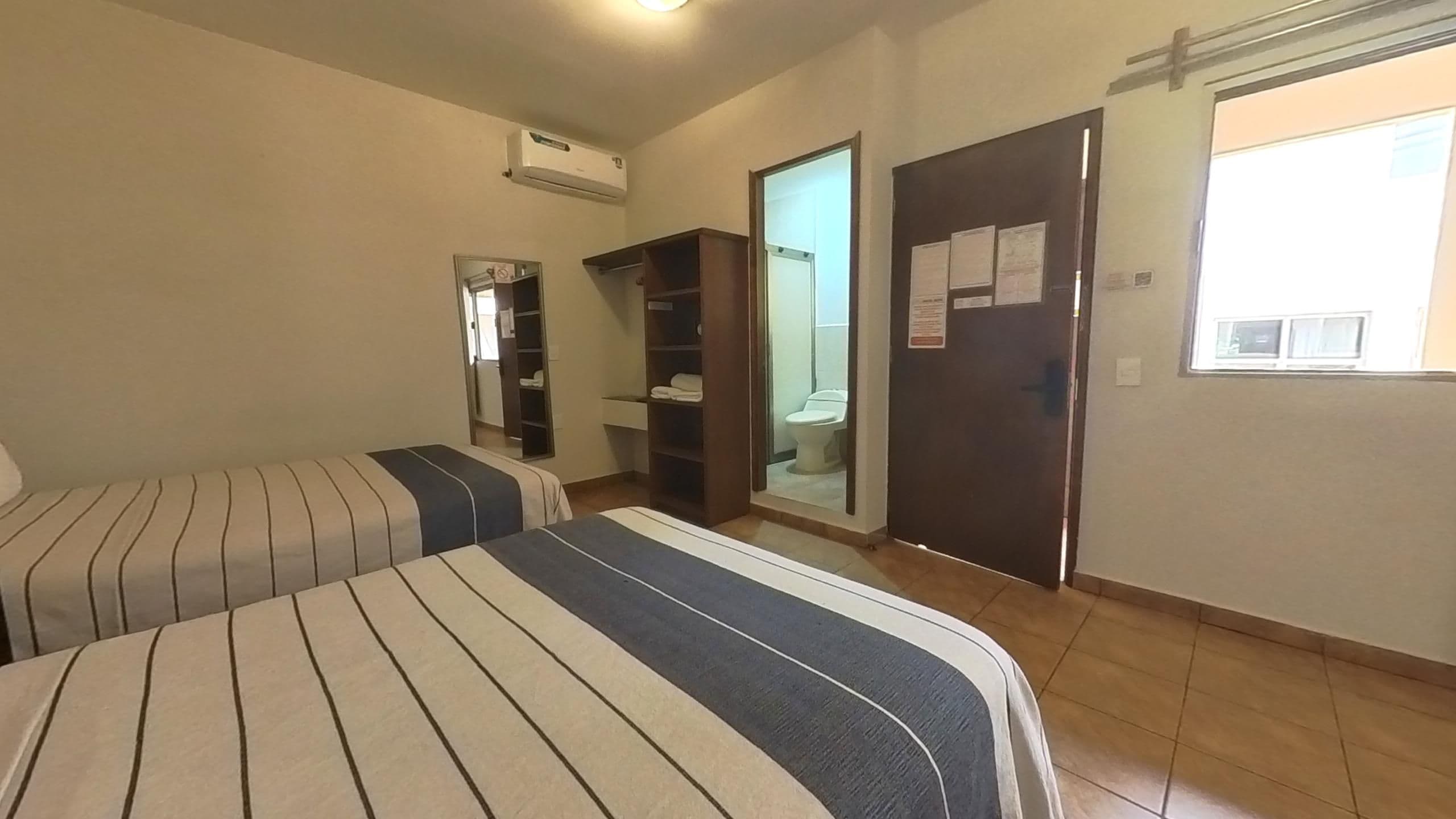 Hotellihuone, jossa on kaksi sänkyä, vaatekaappi ja kylpyhuone, jossa on wc ja pesuallas, sekä ilmastointilaite.
