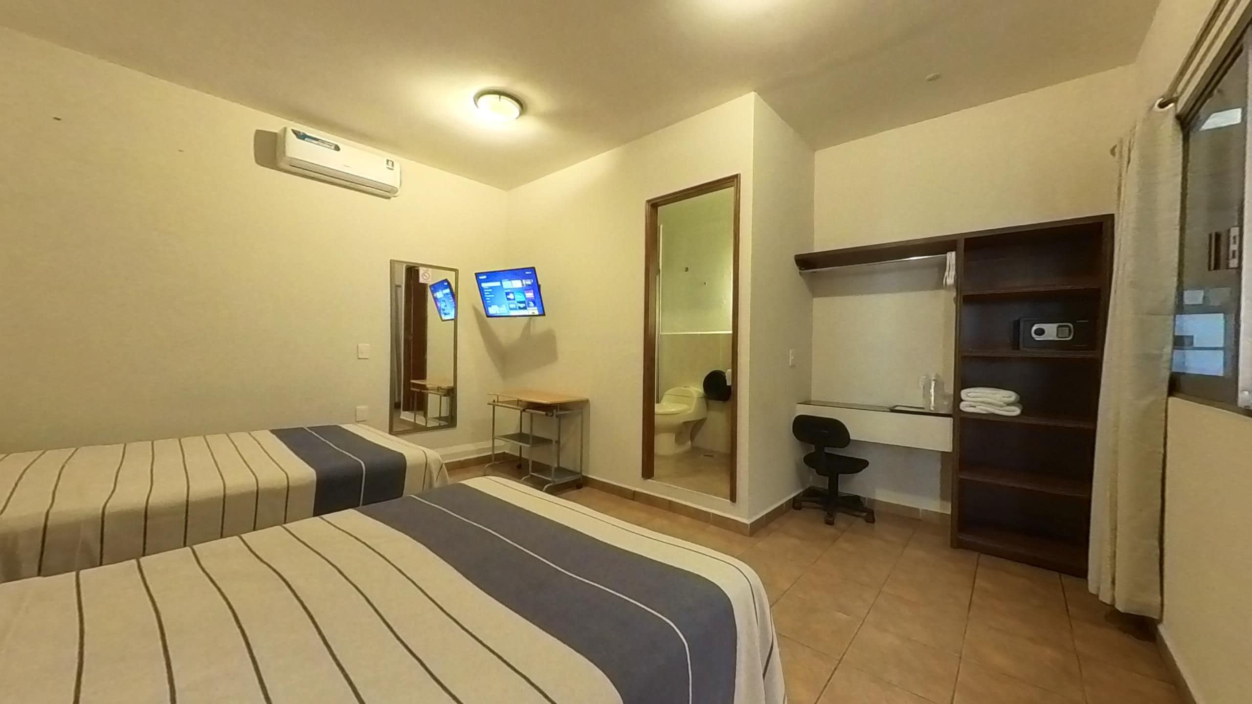 A hotel room with two beds, a desk, a chair, a wardrobe, a mirror, and a television.