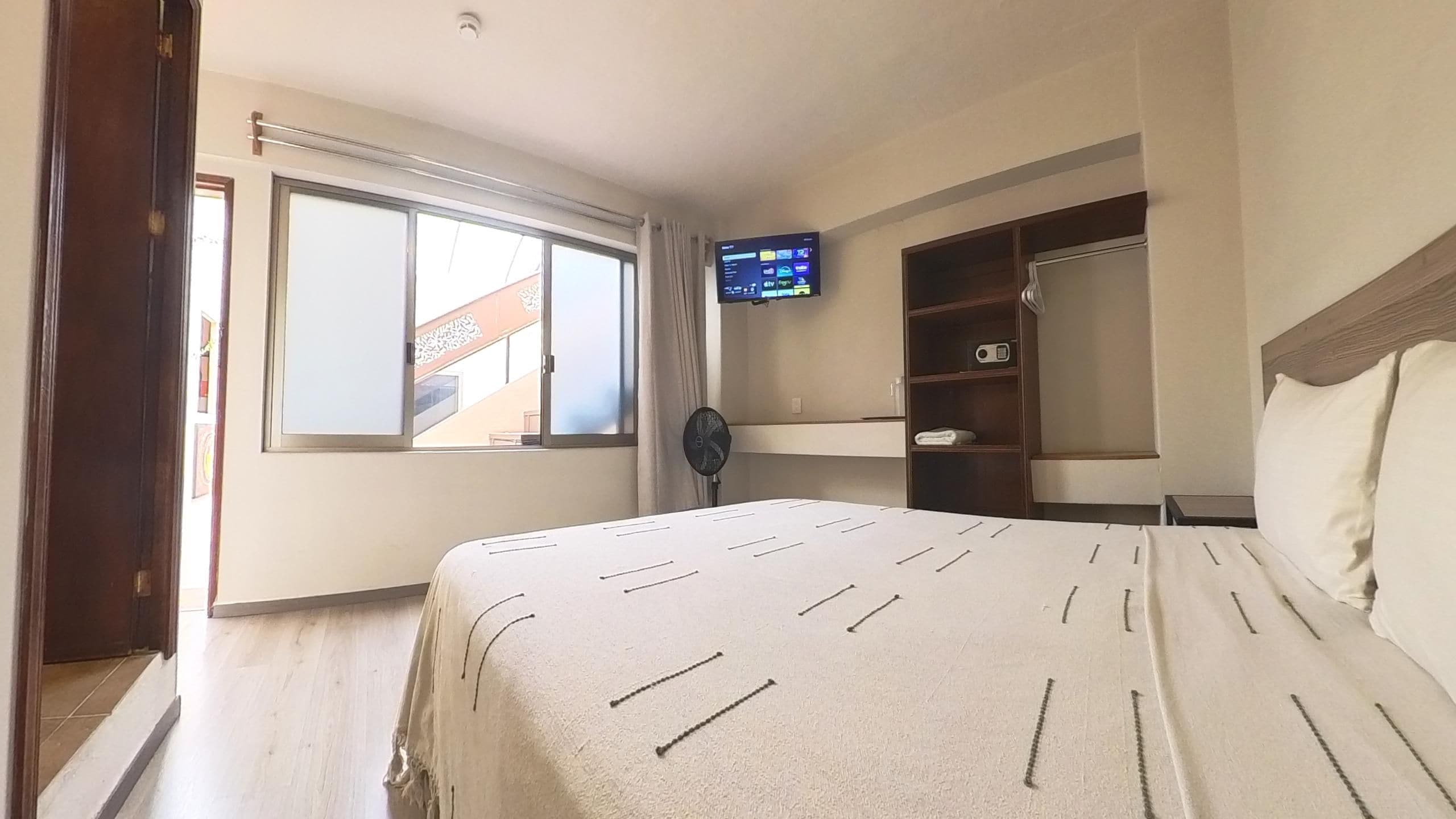 A bedroom with a bed, a TV mounted on the wall, and a window.