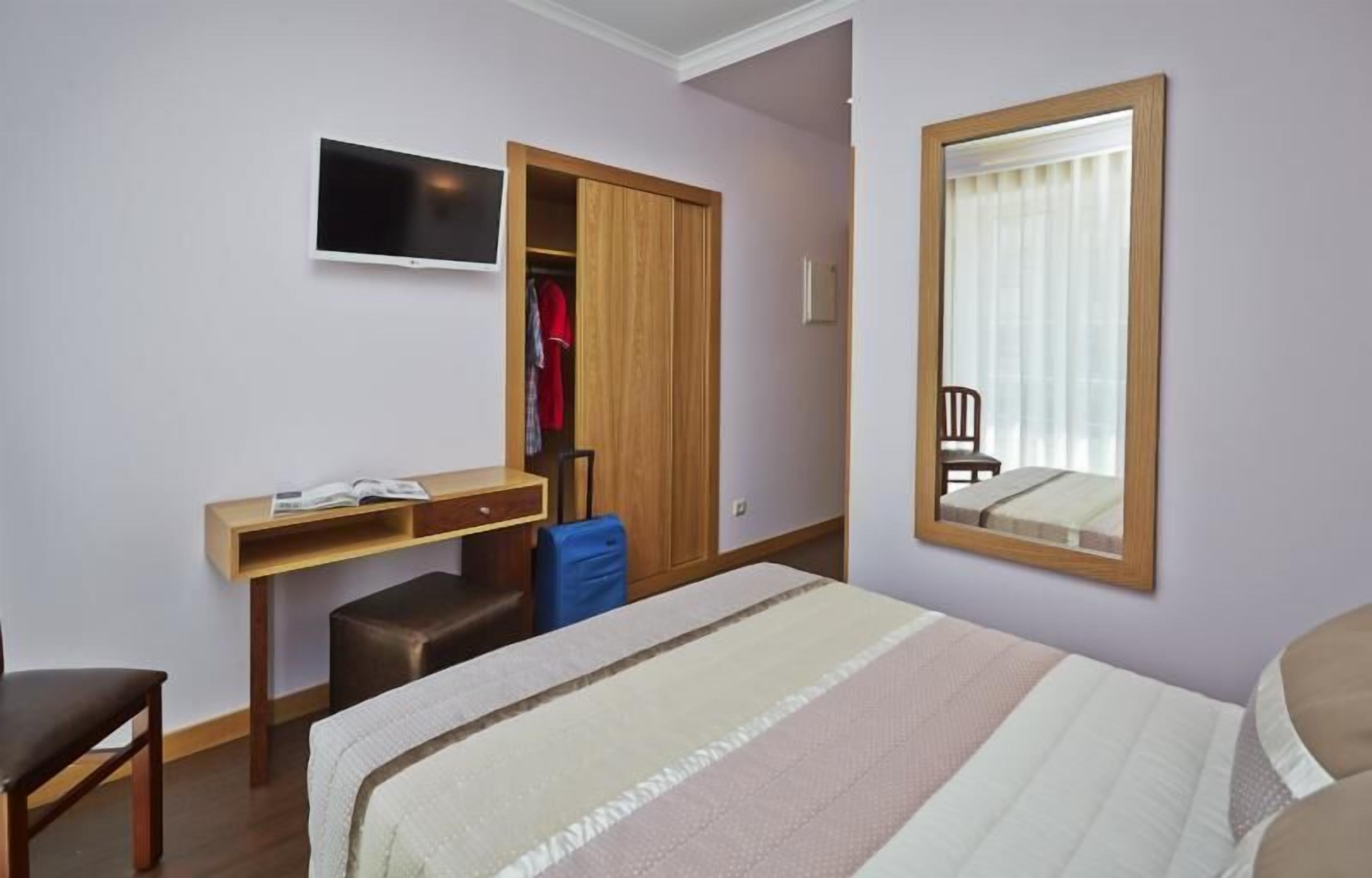 Habitación de hotel con cama, escritorio con silla, televisor, armario y ventana con espejo.