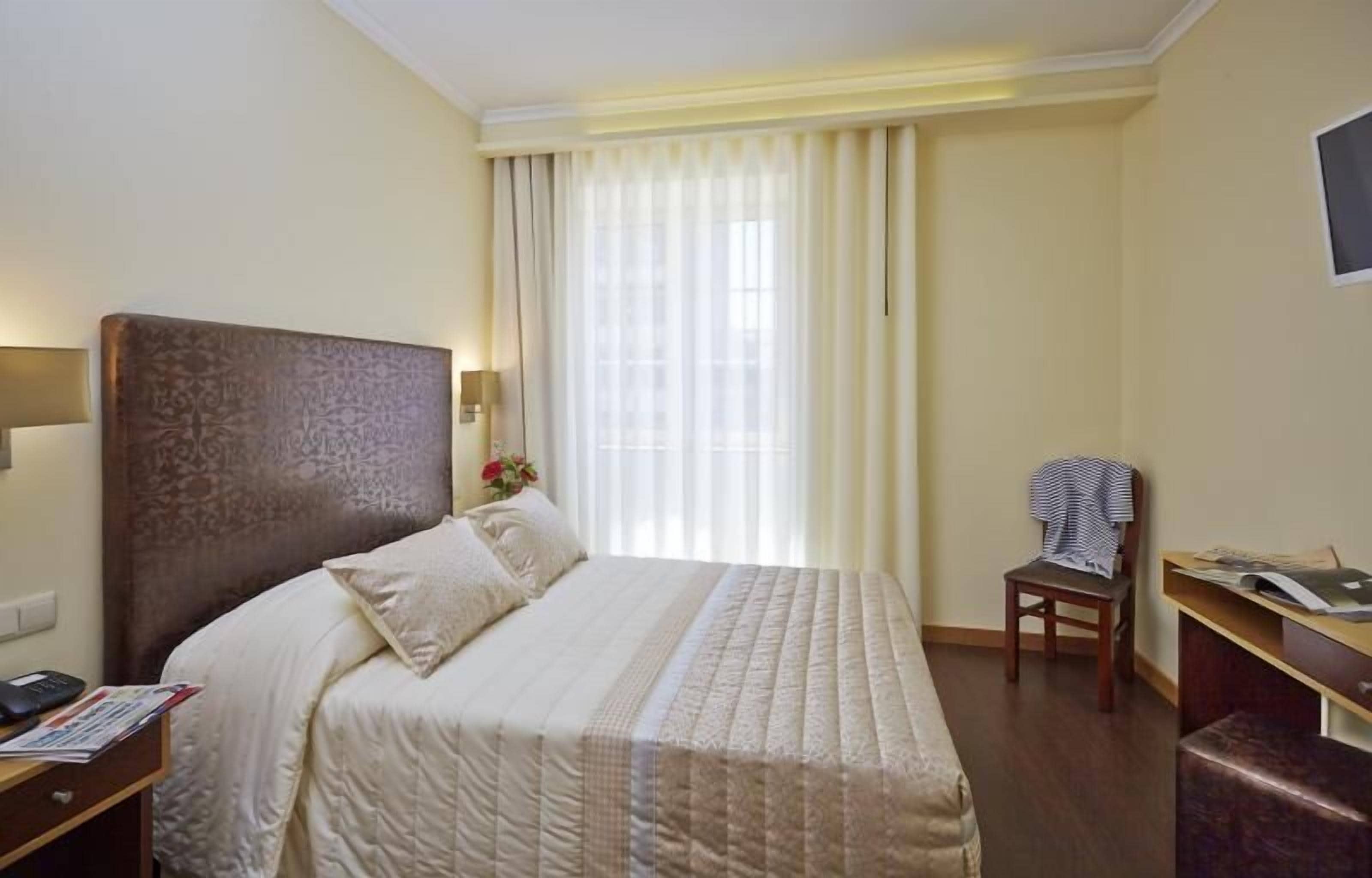 A hotel room with a large bed, a desk, a chair, and a window with curtains.