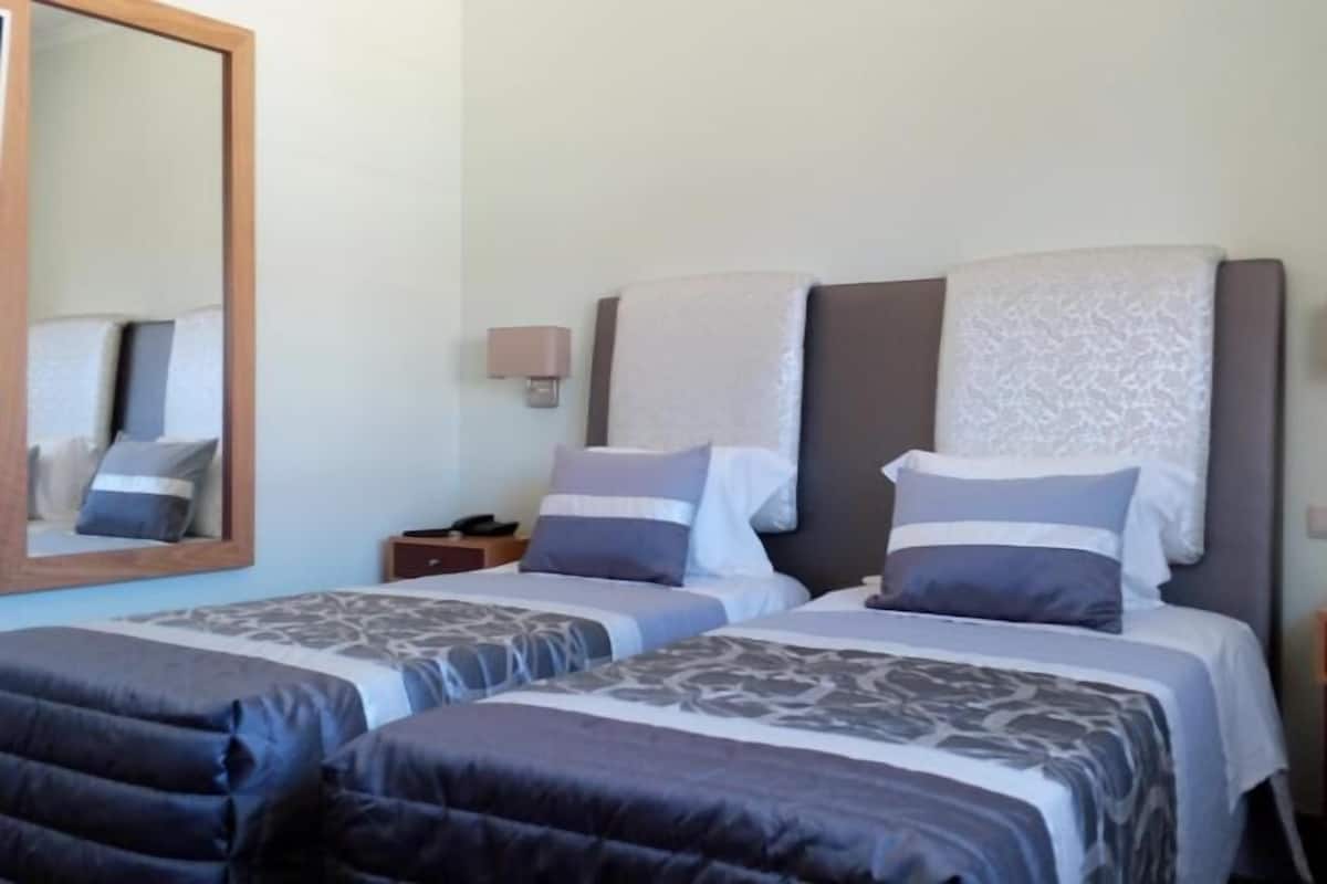 A hotel room with two beds, a large mirror, bedside lamps, and a nightstand.