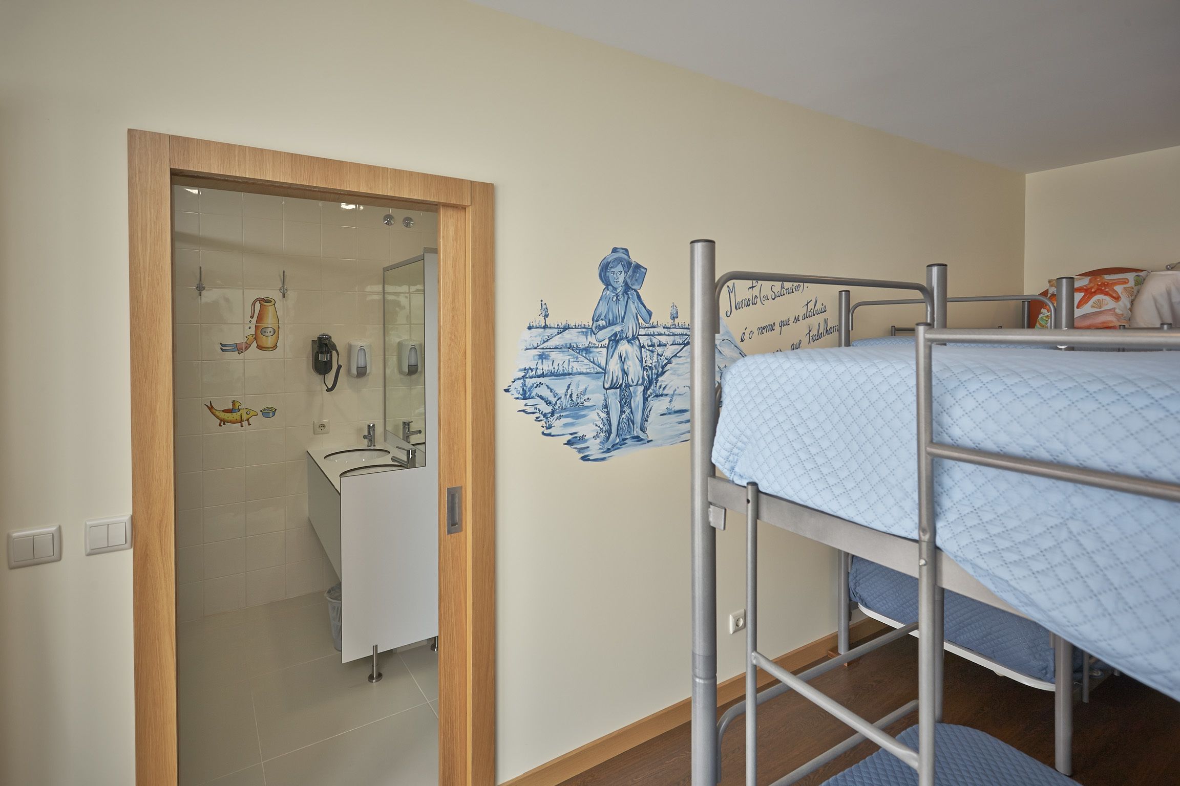 A room with bunk beds, a bathroom with a sink, and a wall with a mural.