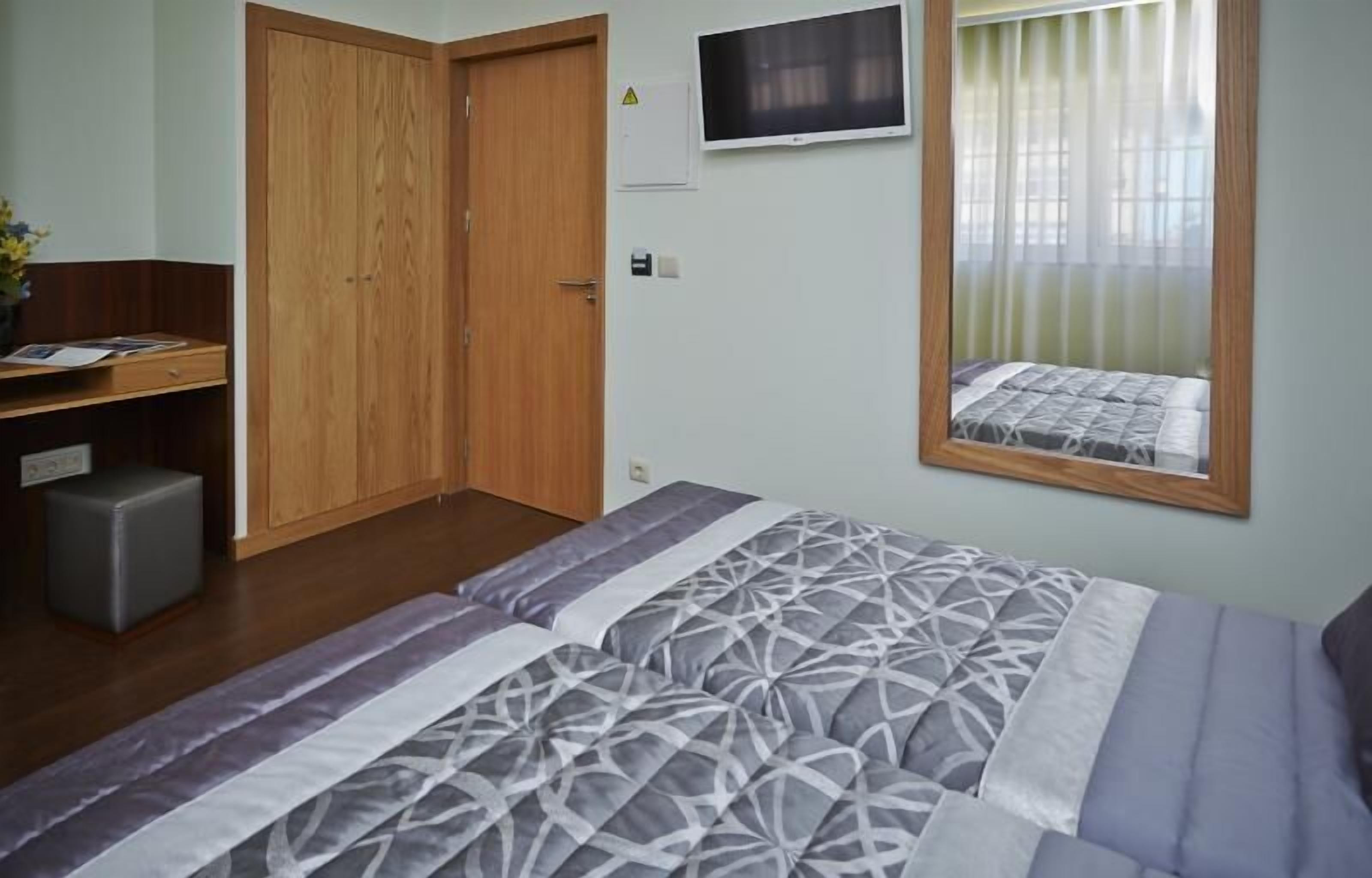 A bedroom with a bed, a desk, a wardrobe, a television, and a window with curtains.