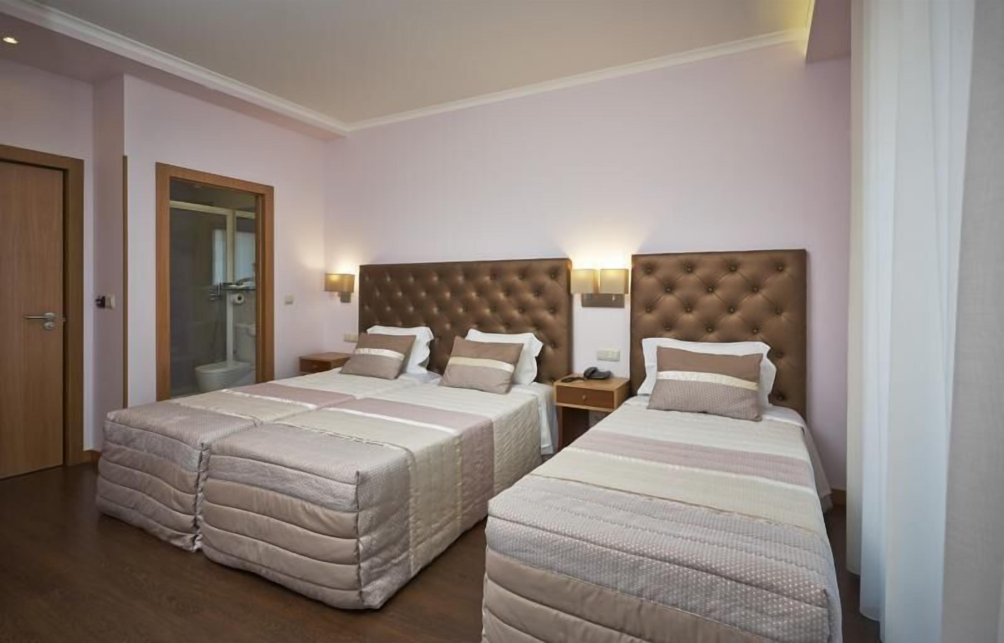 A hotel room with two beds, each with a headboard and bedside lamps.