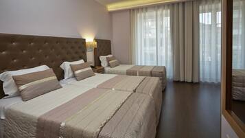 A hotel room with two beds, a large window with curtains, and a modern headboard.