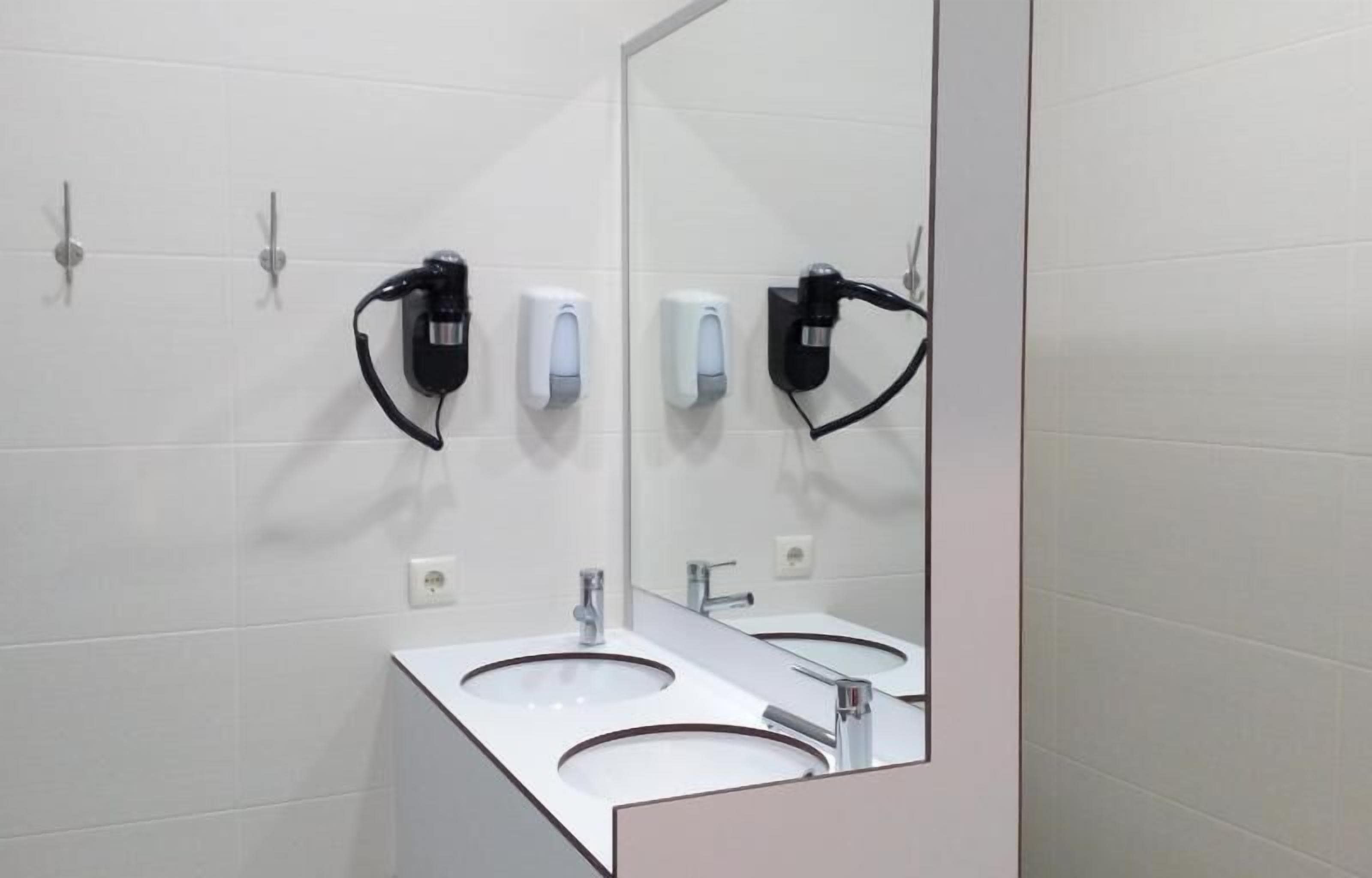 Un baño moderno con dos lavamanos, un espejo grande y secadores de pelo fijos en la pared.