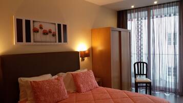 Una habitación de hotel con una cama, una silla, un cuadro y una ventana con cortinas.
