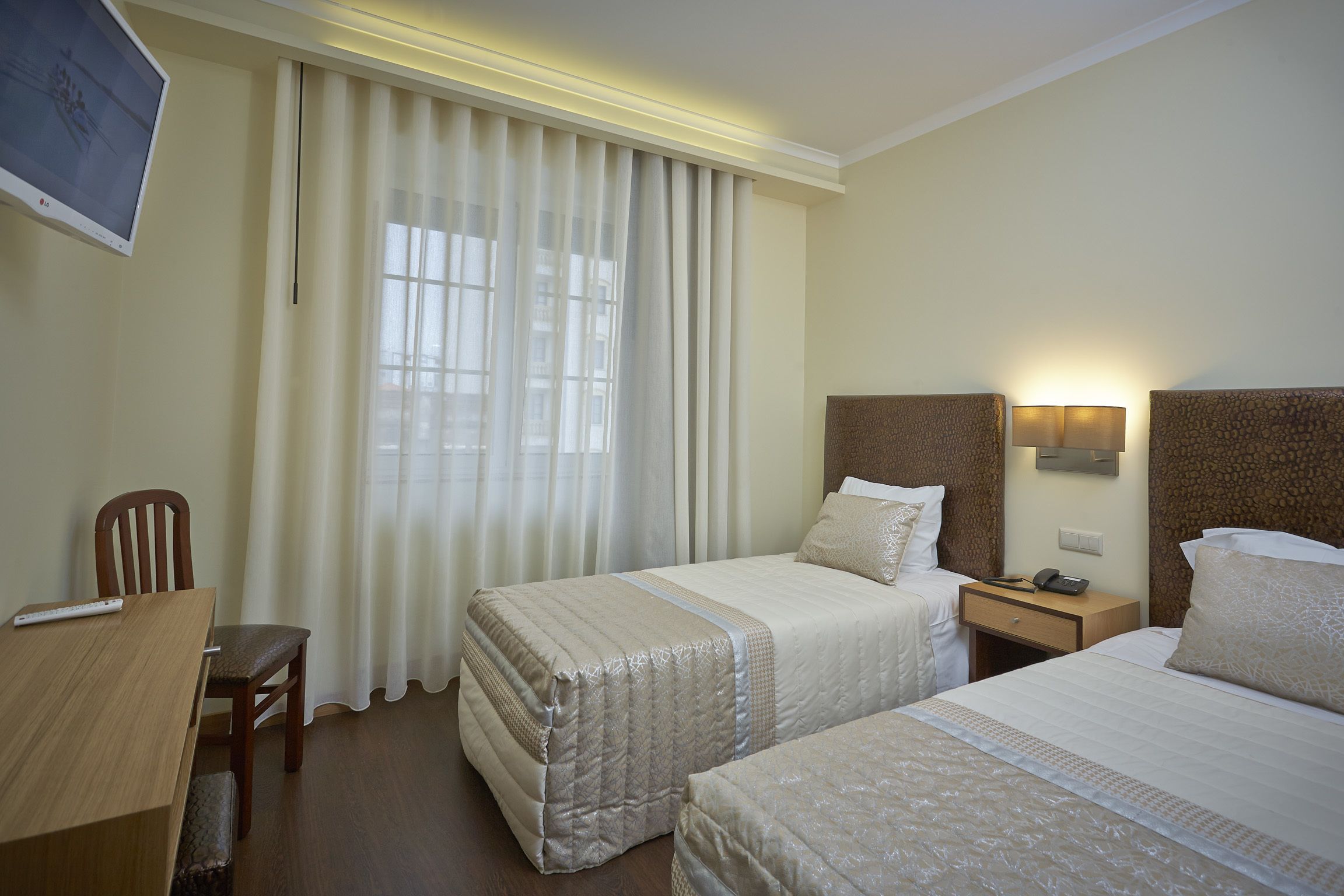 A hotel room with two beds, a desk, a chair, a TV, and a window with curtains.