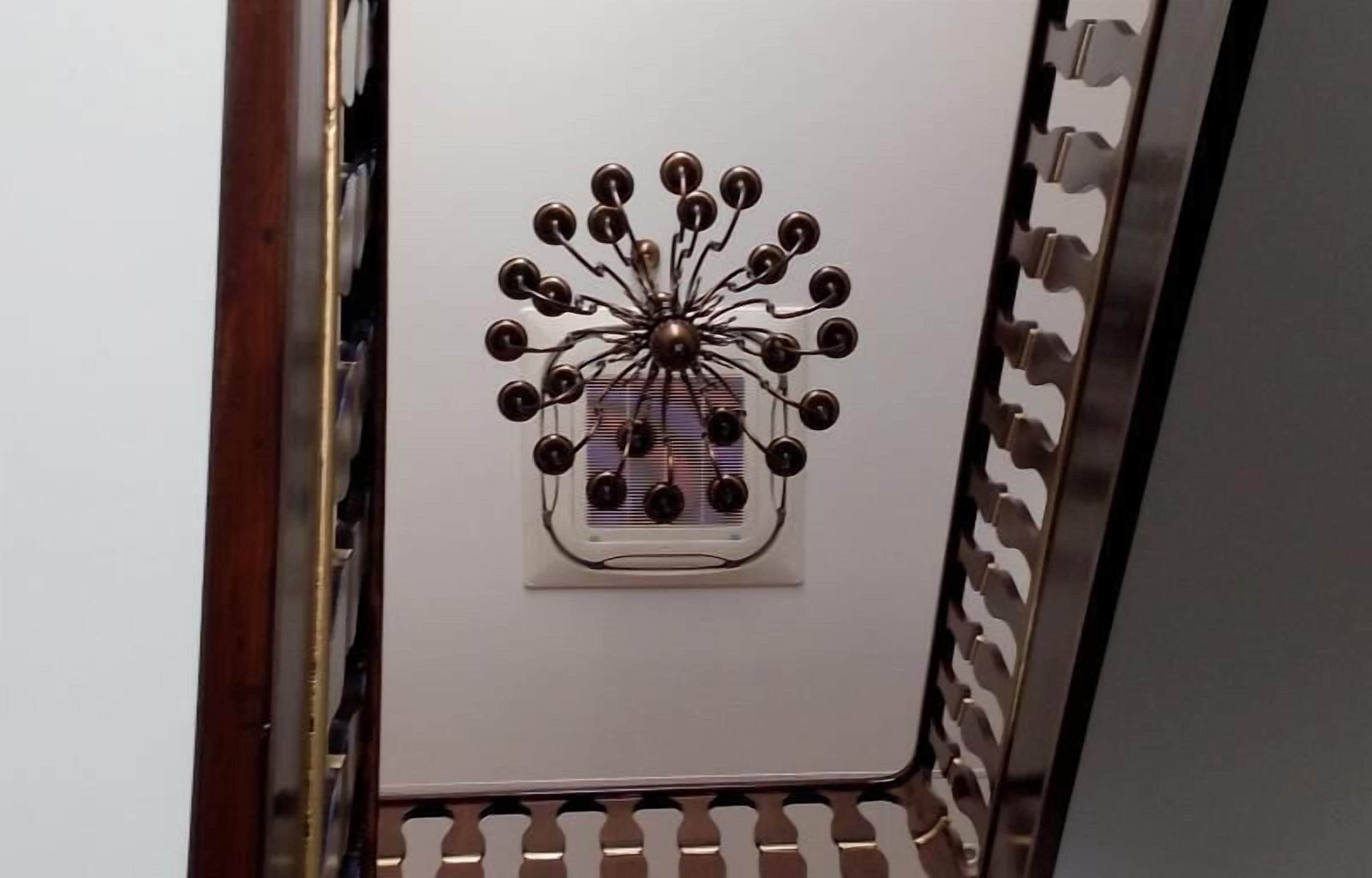 Un objeto metálico y circular con un eje central y elementos que irradian, posiblemente una pieza decorativa o parte de un mueble.