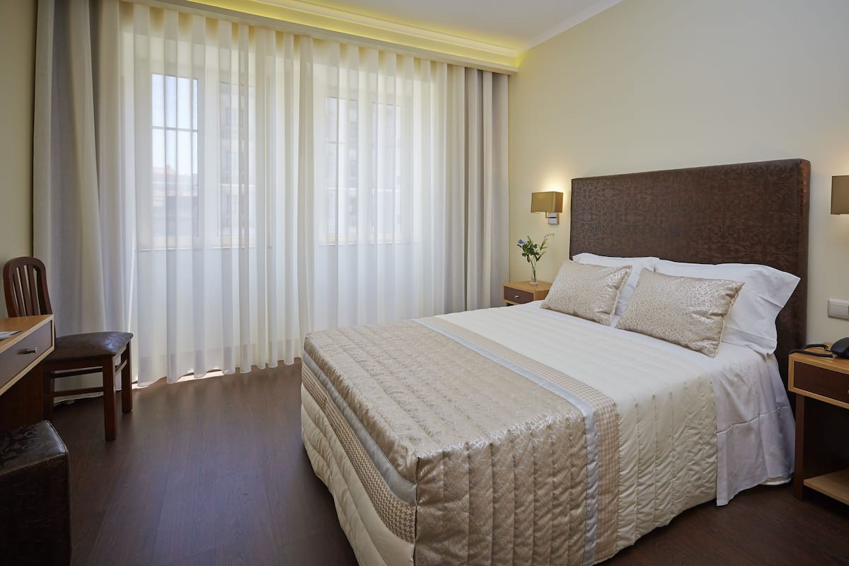 A hotel room with a large bed, a desk, a chair, and a window with curtains.