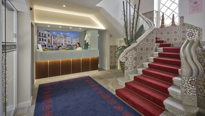 A hotel reception area with a modern desk, a staircase with red carpet, and a decorative wall with patterned tiles.