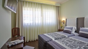 A hotel room with two beds, a TV mounted on the wall, a desk with a newspaper, and a chair.